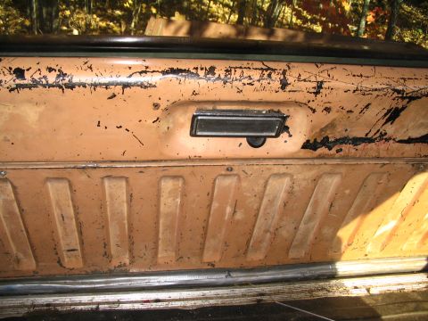 1984 Ford Bronco - Close-up of a worn orange interior door panel, showing a black handle and textured lower section.