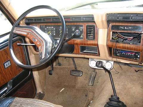 1984 Ford Bronco - The interior of a truck, wood grain trim and an XLT badge on the dashboard, shows signs of wear and modification.