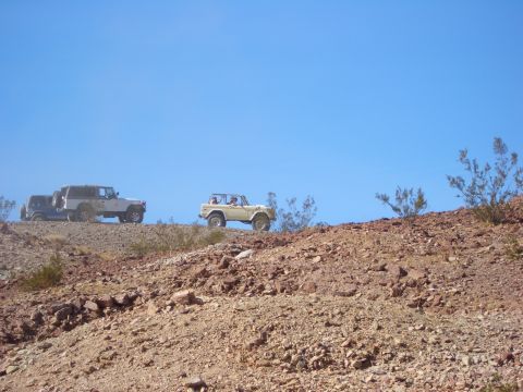 1985 Ford Bronco - Several off-road vehicles traverse a rocky desert landscape under a clear blue sky.