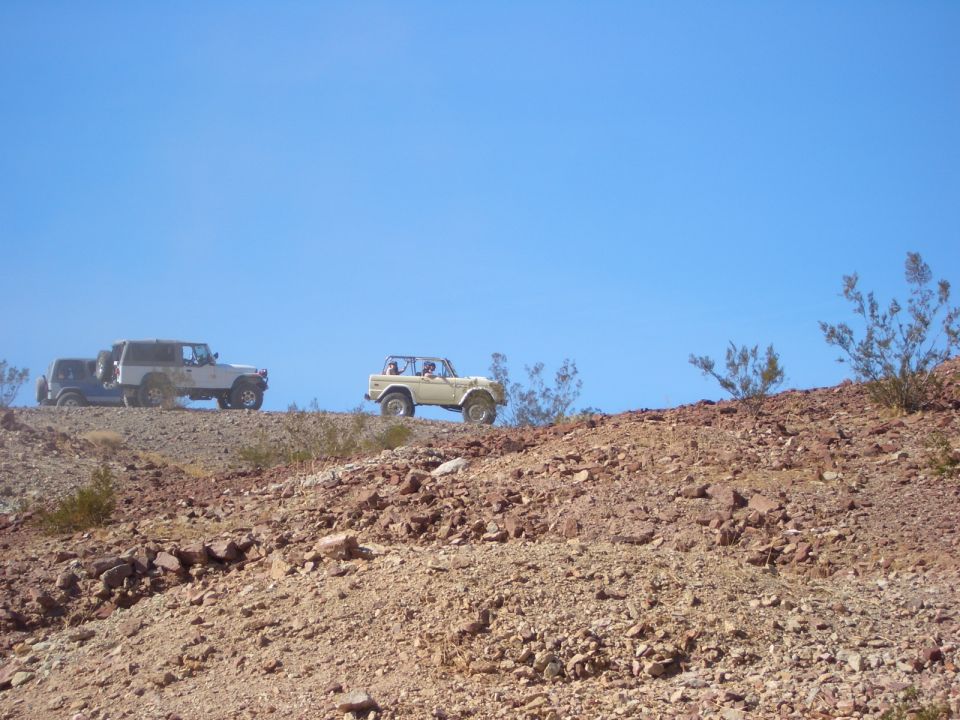 1985 Ford Bronco driving on a desert hill with two other SUVs behind it