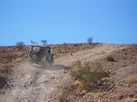 1985 Ford Bronco - A Jeep Wrangler navigates a challenging off-road trail in a desert landscape.