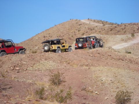 1985 Ford Bronco - Several off-road vehicles navigate a rocky, desert terrain on a sunny day.