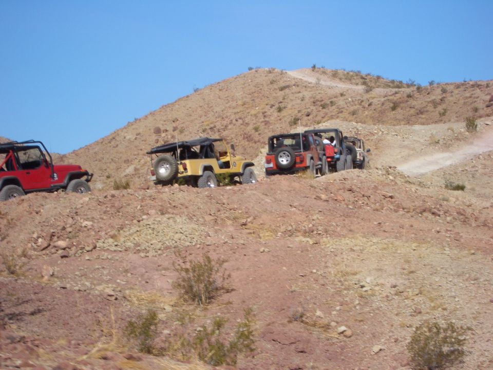 Four-wheel drive vehicles on a dusty, arid hillside under a clear blue sky