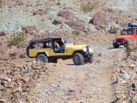 1985 Ford Bronco - Two Jeeps navigate a rough, rocky terrain on an off-road trail.