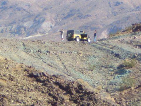 1985 Ford Bronco - A yellow Jeep Wrangler is parked on a rocky, arid landscape with two people observing the surroundings.