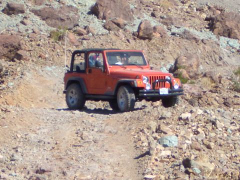 1985 Ford Bronco - An orange Jeep Wrangler navigates a challenging, rocky terrain on an off-road adventure.
