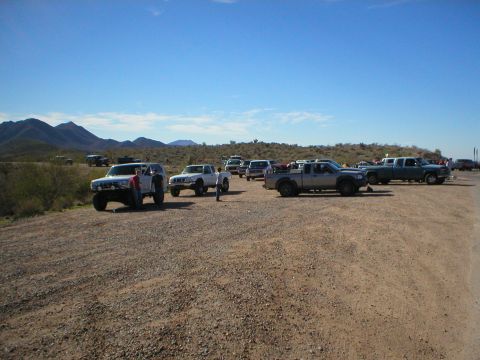 1993 Ford Bronco - A white 1993 Ford Bronco is parked in a dirt lot alongside several other trucks and SUVs under a clear blue sky.