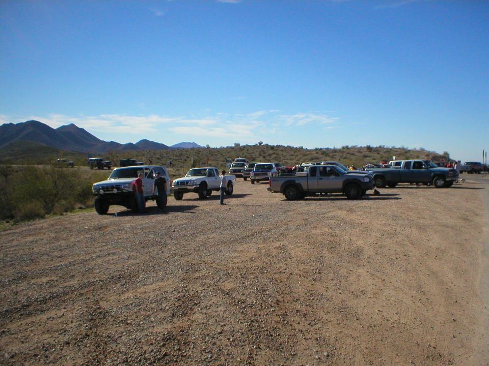 Lifted 4x4s and pickups staged on a desert gravel lot before a trail run