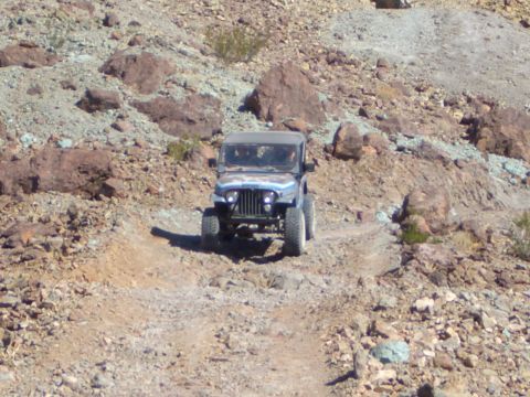 1985 Ford Bronco - A blue Jeep CJ-7 navigates a challenging rocky terrain on an off-road trail.