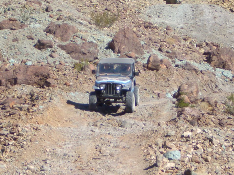 Blue Jeep CJ-7 driving on a rocky, off-road trail