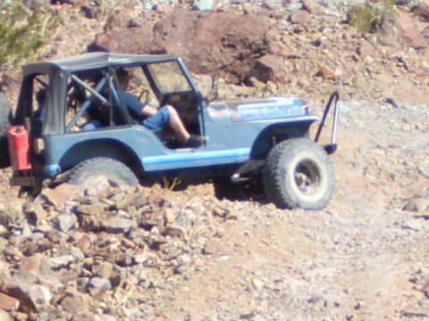 1985 Ford Bronco - A blue Jeep CJ-7 navigates a rocky trail, with a person inside driving.