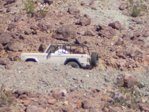 1985 Ford Bronco - A tan Ford Bronco is partially submerged in a rocky ravine, its tires sunk deep into the dirt.