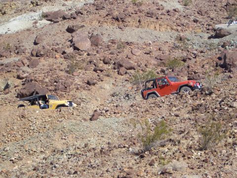 1985 Ford Bronco - Two Jeeps tackle a challenging rocky incline, demonstrating off-road capability.