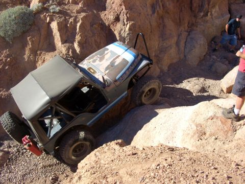 1985 Ford Bronco - An off-road vehicle maneuvers through a challenging rocky terrain, with two people observing.