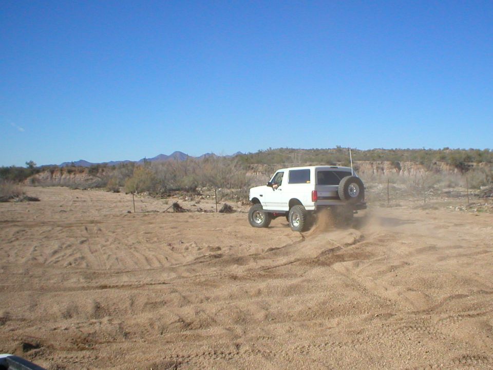 White lifted two-door SUV throwing sand in the desert with rear spare tire