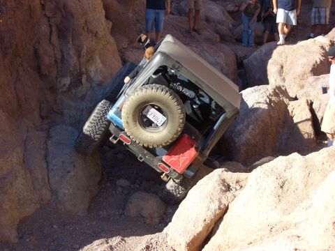1985 Ford Bronco - Jeep Wrangler navigating a rocky trail, showing its rear and spare tire.