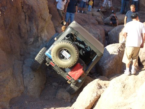 1985 Ford Bronco - A Jeep navigates a rocky off-road trail, with onlookers observing the challenging terrain.