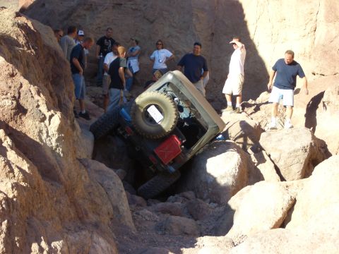 1985 Ford Bronco - A group of people observe a Jeep Wrangler stuck in a rocky off-road trail.