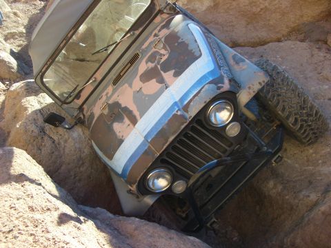 1985 Ford Bronco - Jeep CJ-7 with camouflage paint is stuck between rocks on an off-road trail.
