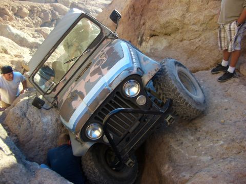1985 Ford Bronco - A Jeep Wrangler is stuck in a tight spot between rocks, with onlookers assessing the situation.