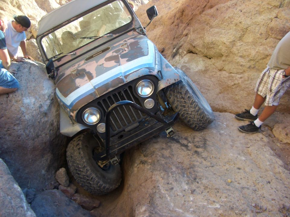 Jeep CJ-7 stuck between rocks on a trail. People are watching