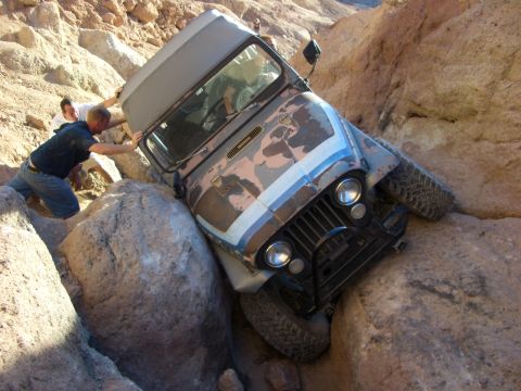 1985 Ford Bronco - A Jeep CJ-7 is wedged between large rocks in a canyon, with two individuals attempting to free it.