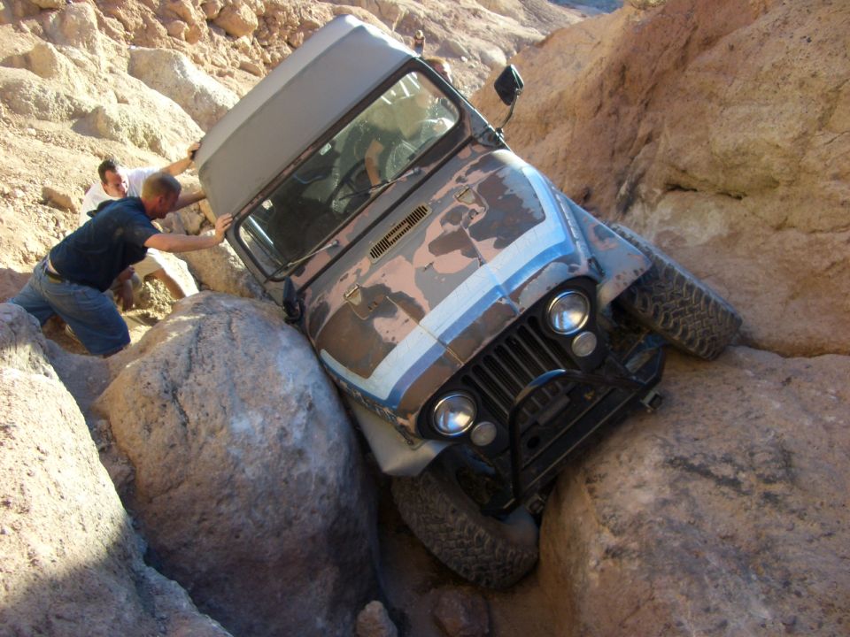Jeep CJ-7 stuck between rocks, two people pushing it