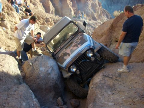1985 Ford Bronco - Off-road vehicle stuck between large rocks with onlookers.