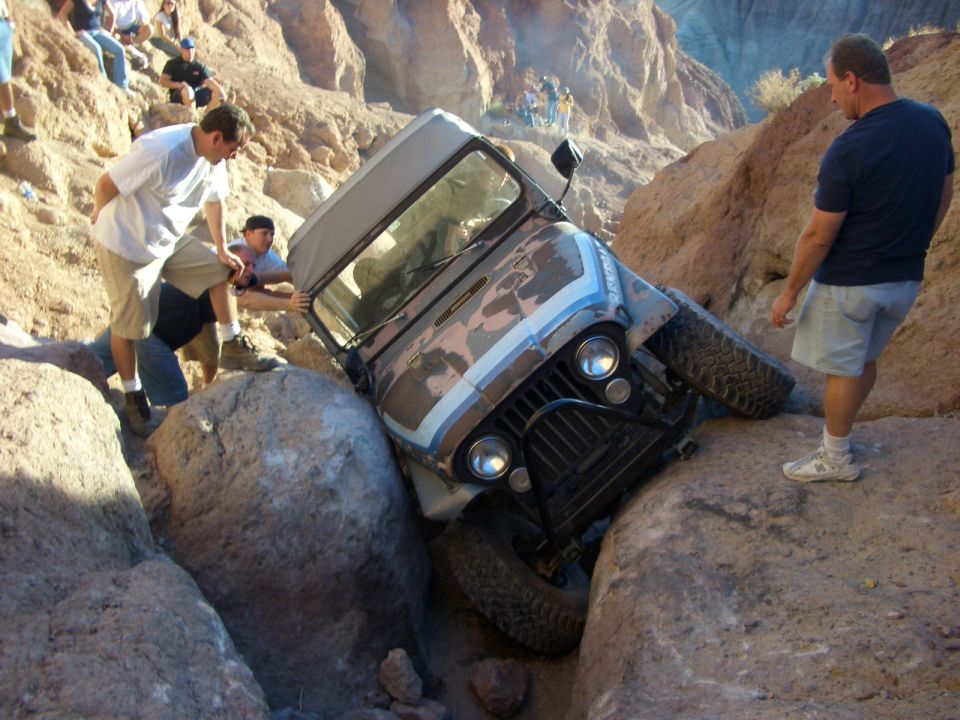 Jeep CJ tilted on rocks with people trying to help it