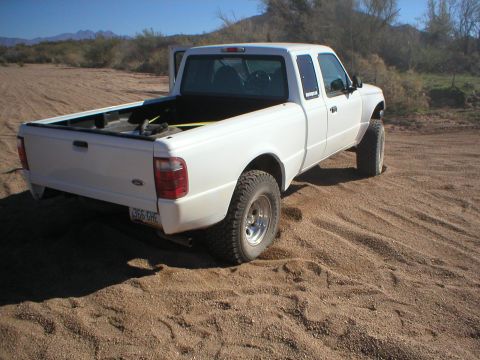 1993 Ford Bronco - A white pickup truck is parked on a sandy surface with dry brush and mountains visible in the distance.