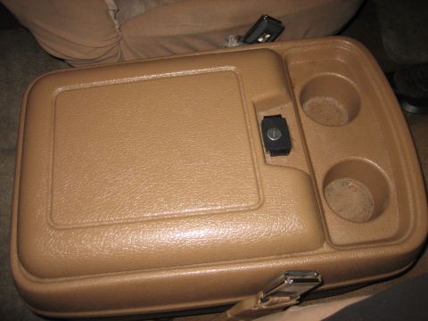 1990 Ford Bronco - Tan plastic center console armrest with two cup holders and a locking storage lid, set on cloth seats.