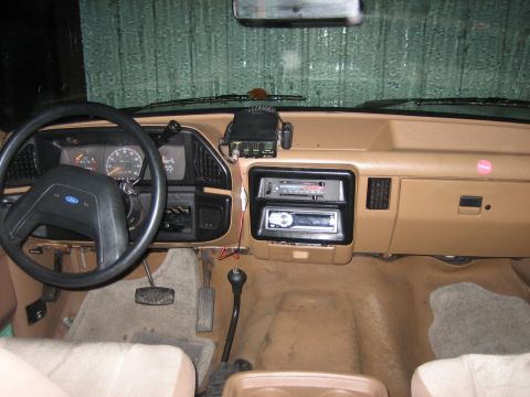 1990 Ford Bronco - The interior of the vehicle shows a tan dashboard with two radios and a CB radio mounted above the dashboard.