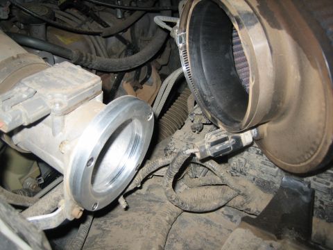 1995 Ford Bronco - Engine-bay close-up of a mass air flow sensor housing with a polished aluminum adapter flange, disconnected from a large black rubber intak…
