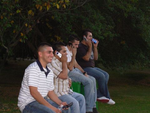 1995 Ford Taurus - A group of men are seated outdoors, engrossed in conversations on their mobile phones.