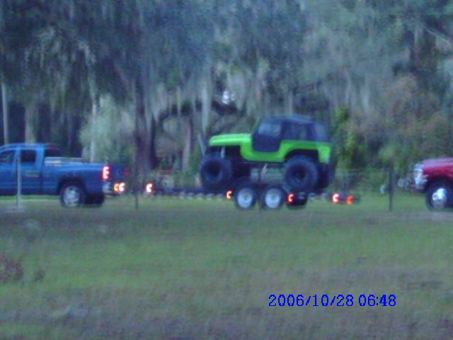 Blue pickup truck towing a trailer with a green off-road vehicle; red vehicle visible on right