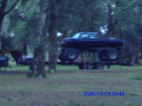 1987 Suzuki Samurai - A black pickup truck with oversized tires is transported on a trailer.