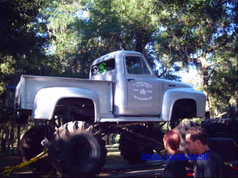 1987 Suzuki Samurai - A modified pickup truck with oversized wheels is parked outdoors under trees.