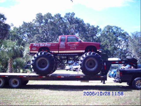 1987 Suzuki Samurai - Monster truck with 'Perry Mud Bogg LLC' text on the side is loaded onto a trailer.