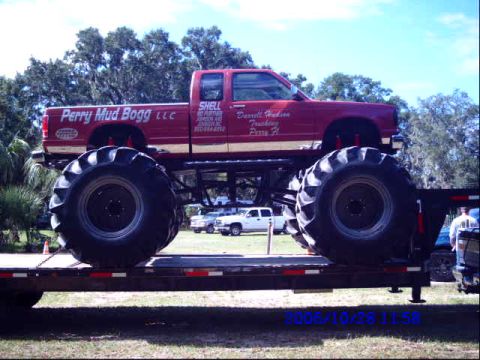 1987 Suzuki Samurai - A custom red monster truck is loaded onto a trailer, with other vehicles visible in the background.