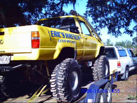 1987 Suzuki Samurai - A yellow lifted pickup truck with "Eric's Wrench Lexus Specialist" written on the side is seen on a trailer.