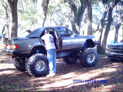 1987 Suzuki Samurai - A lifted sedan with oversized tires is parked outdoors, with another vehicle visible to the right.