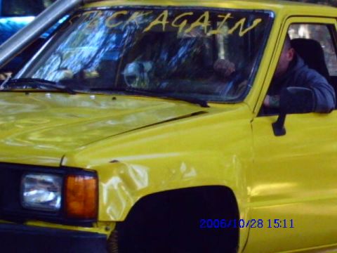 1987 Suzuki Samurai - A yellow truck is seen from the front quarter angle, with text scrawled on its windshield.
