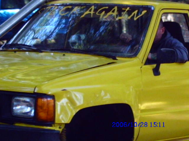 Yellow Toyota pickup truck with crash damage and STUCK AGAIN written on windshield