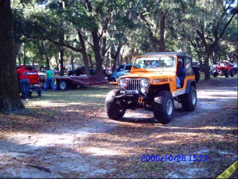 1987 Suzuki Samurai - Orange Jeep CJ-7 parked in a wooded area with other vehicles visible in the background.