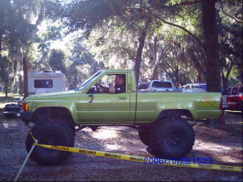 1987 Suzuki Samurai - A heavily modified lime green pickup truck with large off-road tires is parked outdoors.