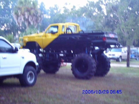 1987 Suzuki Samurai - Monster truck with lifted suspension and large tires parked next to a white pickup truck.