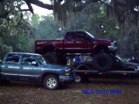 1987 Suzuki Samurai - Two trucks are parked outdoors. One is a blue pickup, the other is a red pickup on a trailer.