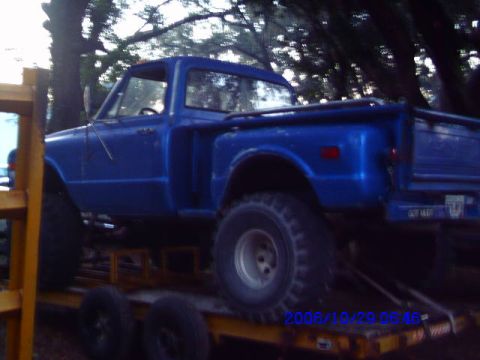 1987 Suzuki Samurai - A blue pickup truck is loaded onto a trailer, viewed from the side with large off-road tires.