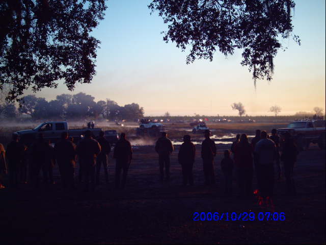 Outdoor gathering with vehicles in the background at sunrise