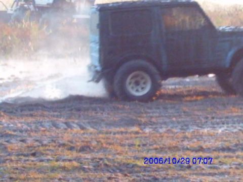 1987 Suzuki Samurai - Vehicle is seen from the side, kicking up a cloud of dust and mud while driving off-road.